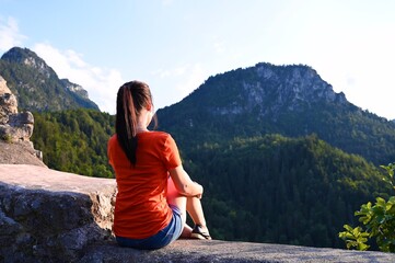 Naklejka premium Young woman sitting on stone watching alpine landscape.