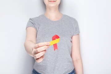 World Hepatitis Day concept. Girl in gray T-shirt holds in her hand awareness symbol red-yellow ribbon. Gray background