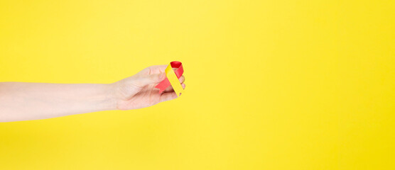 World Hepatitis Day concept. Woman holds in her hand awareness symbol red-yellow ribbon. Yellow background. Copy space