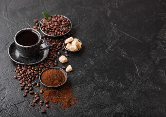 Cup of fresh raw organic coffee with beans and ground powder with cane sugar cubes with coffee tree leaf on black background. Top view