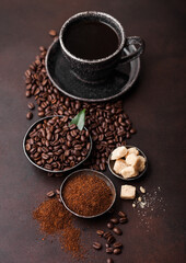 Cup of fresh raw organic coffee with beans and ground powder with cane sugar cubes with coffee tree leaf on brown background. Top view