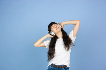 Listening to music in headphones. Portrait of young asian woman isolated on blue studio background. Beautiful cute girl in casual. Human emotions, facial expression, sales, ad, online shopping concept