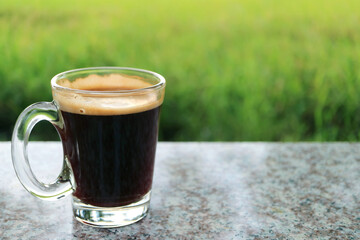 One Hot Black Coffee in a Transparent Glass with Blurry Green Meadow in Background
