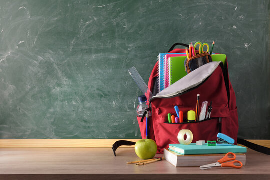 Backpack full of school supplies on table and blackboard front
