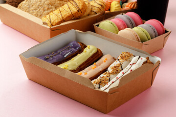 Carton boxes with eclair cakes and cookies on pink surface