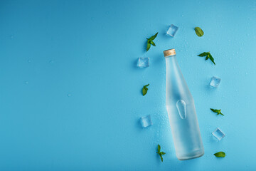 Bottle with an ice cold beverage, ice cubes, drops and mint leaves on a blue background.