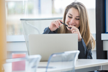 giovane manager bionda è seduta nella sua poltrona di lavoro davanti alla scrivania con il portatile e fa un bel sorriso 