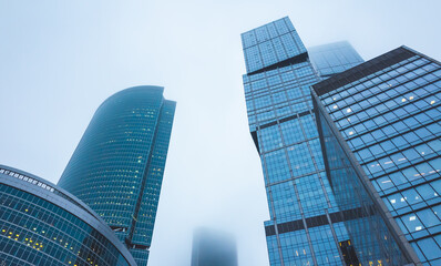 Fototapeta na wymiar Skyscrapers of the office center made of glass and concrete in clouds of thick fog.