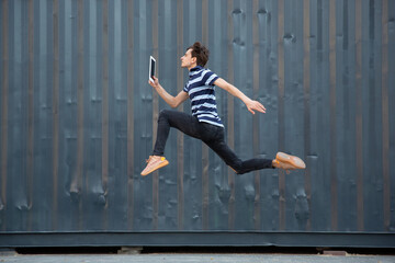 Jumping young buinessman in front of city building wall, on the run in jump high. Reading news,...