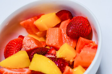 Bowl with assorted delicious tropical fruit. Mango, papaya and strawberries isolated on white background. Healthy snack