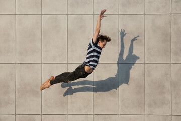 Jumping young buinessman in front of city building wall, on the run in jump high. Hurrying up,...