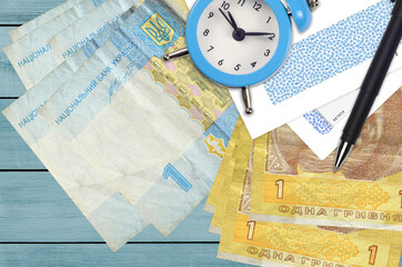 1 Ukrainian hryvnia bills and alarm clock with pen and envelopes. Tax season concept, payment deadline for credit or loan. Financial operations using postal service