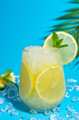 Lemonade frappe with round slice of lemon and mint on blue ice background. Mojito frappe in glass with copy space.. 