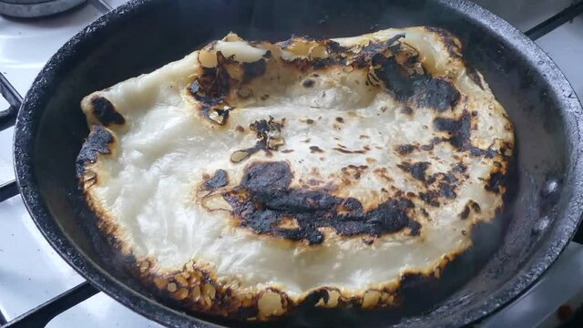 Traditional tasty Indian Partha hot charred smoking pancake cooking on stove in pan dolly left