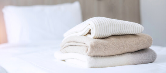 Stack of beige wool Sweaters on bed in luxury hotel or resort or home. Relax, autumn or winter clothes, laundry and vacation concepts