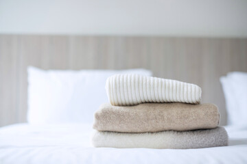Fototapeta na wymiar Stack of beige wool Sweaters on bed in luxury hotel or resort or home. Relax, autumn or winter clothes, laundry and vacation concepts