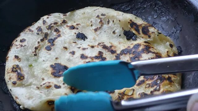 Checking and turning traditional charred tasty Indian Partha hot pancake cooking on stove in pan