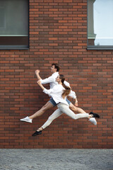 One way to go. Jumping young couple in front of city building wall, on the run in jump high....