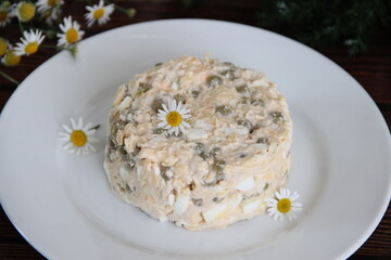 Salad with canned fish, eggs and canned peas, decorated with flowers, on a white plate