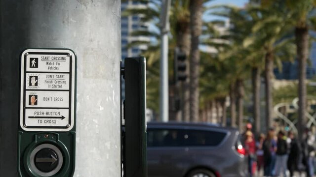 Traffic light button on pedestrian crosswalk, people have to push and wait. Traffic rules and regulations for public safety in USA. Zebra street crossing on road intesection in San Diego, California.
