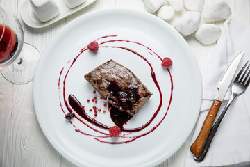 Venison meat with raspberry sauce on a white plate. On a white wooden table.
