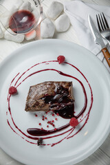 Venison meat with raspberry sauce on a white plate. On a white wooden table.
