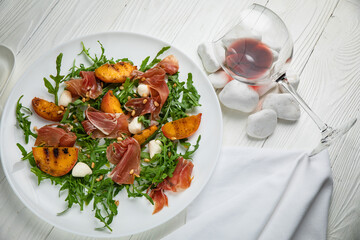 Jamon with arugula and peach on a white plate. On a white wooden table.
