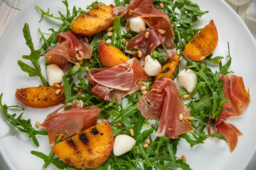 Jamon with arugula and peach on a white plate. On a white wooden table.

