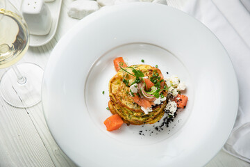 Pancakes with salmon, cheese, herbs. On a white wooden table
