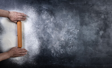 Man hands keep rolling pin with flour on dark table, top view