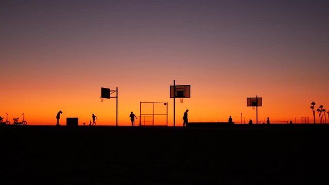 California summertime dusk beach aesthetic, pink sunset. Unrecognizable silhouettes, people play game with ball on basketball court. Newport ocean resort near Los Angeles CA USA. Purple sky gradient.
