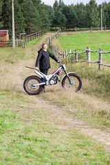 Fototapeta premium Dirt countryside road with mature Caucasian woman standing with motorcycle