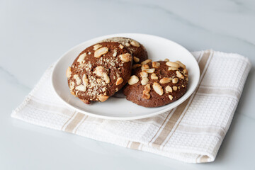chocolate chip cookies with nuts and peanuts in a white tea plate on a table with a tea napkin