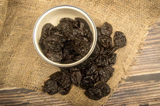 Dried prunes in a metal bowl and dried prunes scattered on a background of coarse-textured burlap. Close up.