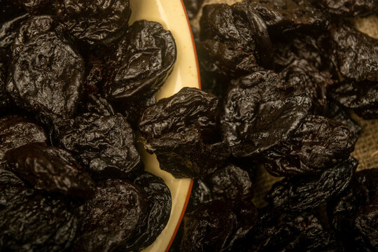 Dried prunes in a ceramic bowl and dried prunes scattered on a background of coarse-textured burlap. Close up.