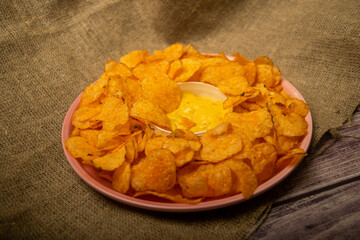 Potato chips on a round platter and a saucepan with cheese sauce. Close up.