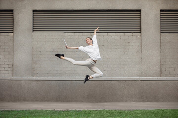 Using tablet. Jumping young woman in front of city building wall, on the run in jump high. Hurrying...