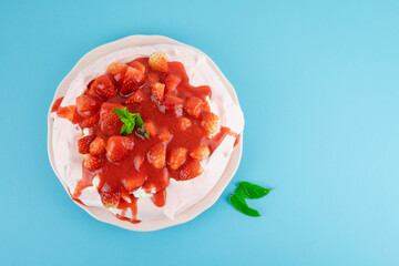 Pavlova with red fruits on a blue background. Copy space. Pastry concept.