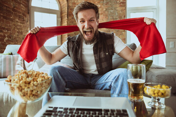 Excited football fan watching sport match at home, remote support of favourite team during...
