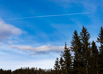 condensation trail and clouds over the forest on blue sky