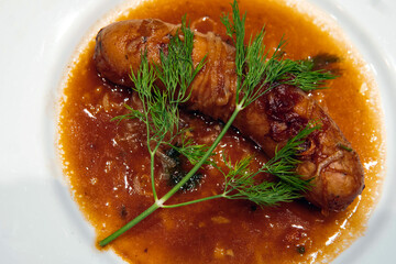Grilled smoked sausage with gravy and dill on top  on the white dish.  Delicious sausage  and  brown sauce.