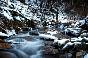 semi frozen small waterfall in a stream in the mountains in deep winter with ice