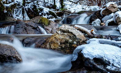 semi frozen small waterfall in a stream in the mountains in deep winter with ice