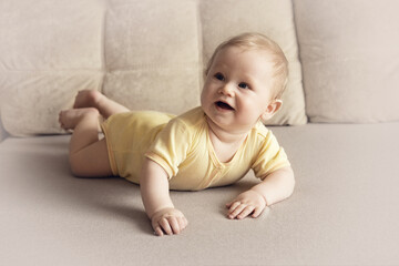 Fototapeta premium Cute six month old baby lying on his stomach on a bed on a beige background. Soft focus, copy space.