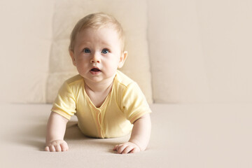Fototapeta premium Cute six month old baby lying on his stomach on a bed on a beige background. Soft focus, copy space.