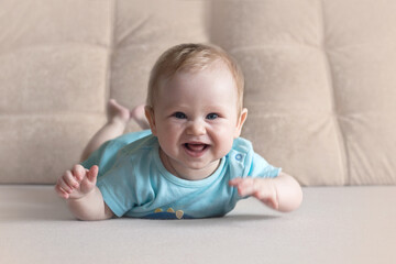 Fototapeta premium Cute six month old baby lying on his stomach on a bed on a beige background. Soft focus, copy space.