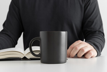 Fototapeta na wymiar Black mug mockup with man reading a book.