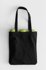 Black tote bag mockup with fruit on a white table.