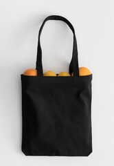 Black tote bag mockup with fruit on a white table.