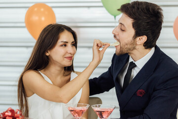 Young caucasian couple at a party together, girlfriend is feeding snacks to her boyfriend.